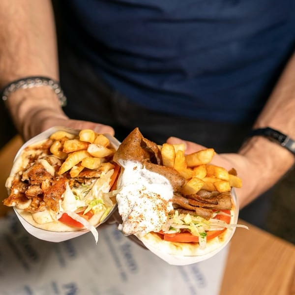 Hands holding two Pita Yeero gyros, one chicken and one beef, filled with fries and sauce.