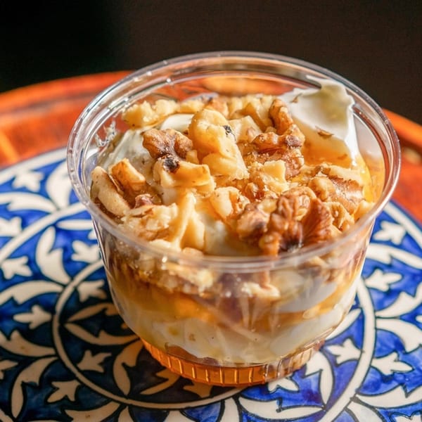Greek yogurt with honey and walnuts in a clear cup on a blue and white patterned plate.