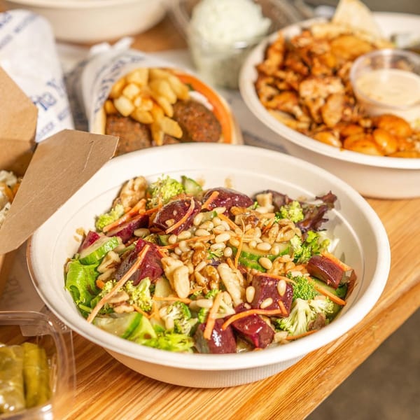 A Pita Yeero salad with beets, broccoli, pine nuts, and walnuts, surrounded by other Greek dishes.