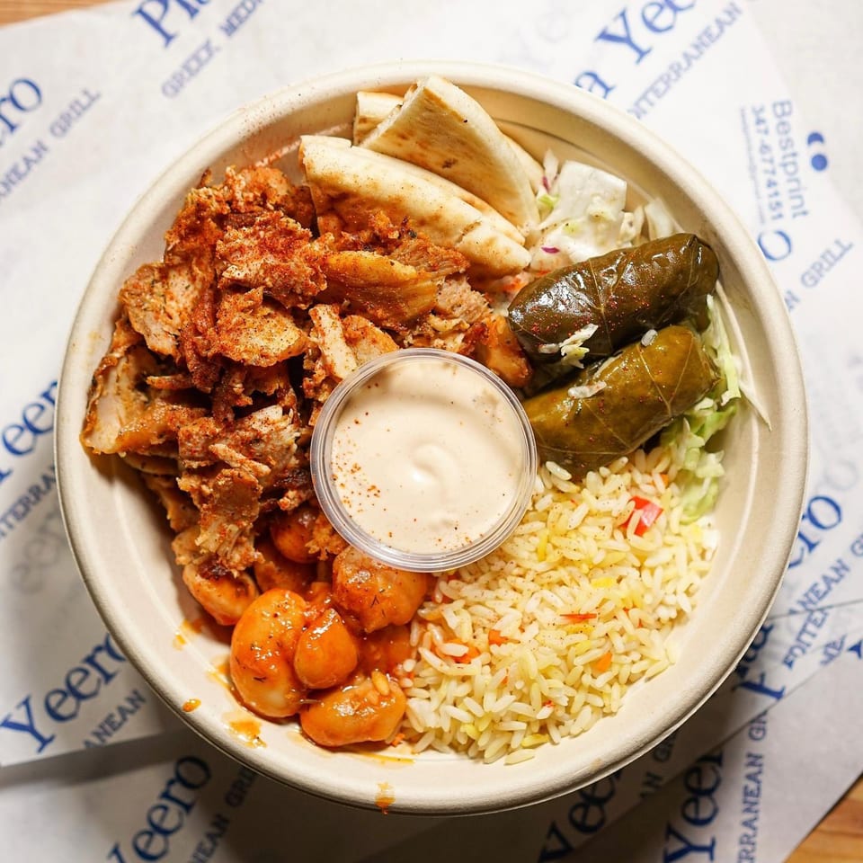 A Pita Yeero bowl with seasoned chicken, rice, pita bread, dolmades, and a side of sauce.