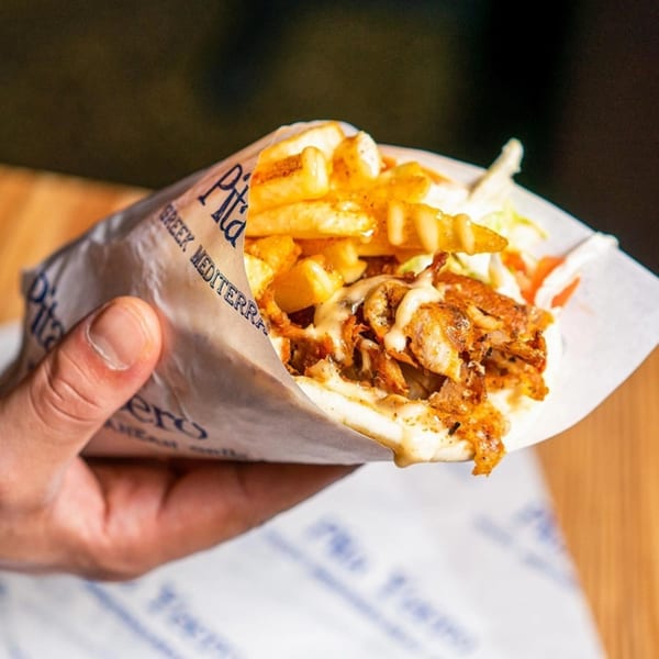Hand holding a Pita Yeero with meat, fries, and sauce wrapped in branded paper.
