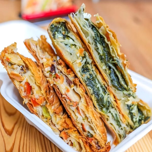 Close-up of two Greek spanakopita and two savory phyllo pastries in a white container.