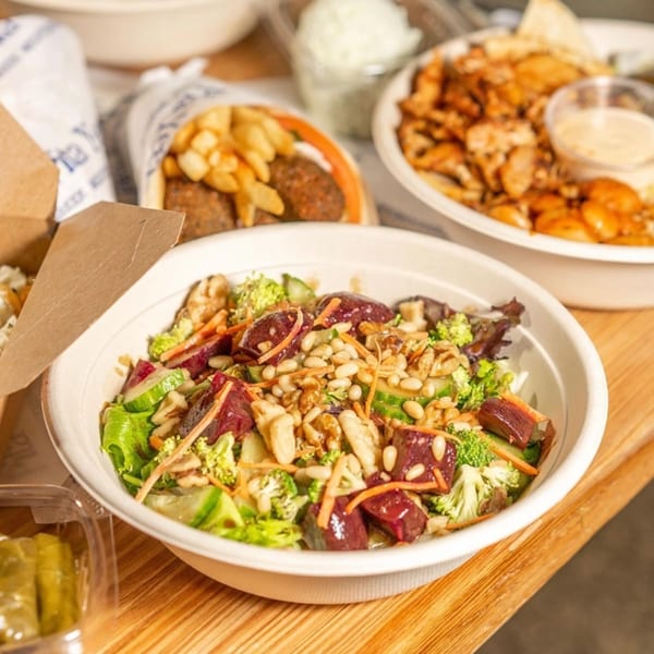 A Pita Yeero Greek salad with beets, broccoli, and pine nuts, surrounded by other Greek dishes.